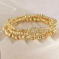 Gestapelte goldene facettierte Perlenarmbänder auf einer weißen strukturierten Keramikschale - 3mm Facettierte Kupferperlen Armband Stapel