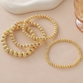 Vierteiliges goldenes Perlenarmband-Set mit eleganter Textur auf beigem Hintergrund - Kürbisperlen Armband Stapel