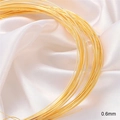 Macro detail of 0.6mm 18K gold-plated jewelry wire coiled on white silk fabric - 0.6