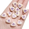 Handheld view of heart-shaped pearlescent acrylic beads with purple iridescent finish - 15x13mm (5 Pieces/Pack) / White with Purple Center