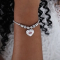 Silbernes Perlenarmband mit Herzanhänger und Evil-Eye-Motiv am Handgelenk einer Frau - Herz Strahlend Rot Böser Blick Stil (E449-Stahlfarbe)