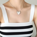 Minimalist silver hollow heart pendant necklace worn on a model with a striped vest - Steel