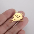 Vue détaillée d'un pendentif chat doré sur le bout du doigt montrant sa petite taille - Ton Or - Chat à Tête Penchée