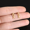 Gold titanium steel ichthys fish stud earrings held by hand for scale on black background - Gold