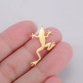 Macro view of gold frog pendant in hand showing tiny dimensions and polished metal finish - Gold