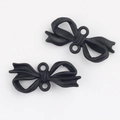 Close-up of matte black bow-shaped charms with dual connector loops for DIY jewelry - Black