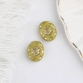 Detail of olive green Czech glass beads with gold floral patterns on a white fabric background - Yellow
