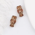 Macro shot of owl-shaped amber glass beads with golden floral textures and drill holes - Brown