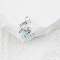 Détail d'un pendentif lune avec rose et émail bleu sur fond de dentelle blanche - Blanc Bleu Argent