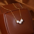 Elegante collar de oro con tres perlas blancas sobre un joyero de cuero marrón oscuro - Perla Artificial Blanca (XL3862) / Chapado en oro 18K
