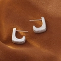 Matte silver geometric J-shaped earrings with a brushed metal finish on brown suede - Thick Silver Brushed
