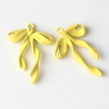 Detalle macro de par de colgantes de lazo en aleación amarillo brillante con cintas fluidas - Amarillo
