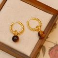 Aros dorados trenzados con colgantes de ojo de tigre sobre un joyero de madera vintage - Pendiente de Ojo de Tigre (Oro 18K)