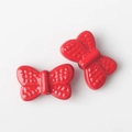 Detail view of two glossy red alloy bow charms with textured wings for jewelry making - Red