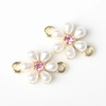 Macro detail of a gold flower charm with white pearl petals and a pink gemstone center - Gold