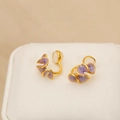 Elegant purple enamel flower ear clips with gold base on a textured jewelry cushion - Taro Purple