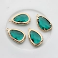 Macro view of four emerald green faceted teardrop pendants with textured gold borders - Peacock Green