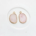 Detail of two irregular pink quartz stone pendants with gold-plated metal frames - Pink