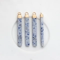 Vista macro di ciondoli in agata blu con punte dorate su un vassoio di ceramica bianca - Ciano