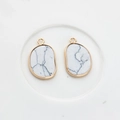 Detail of two irregular white turquoise pendants with gold plated frames on white ceramic - Marble White