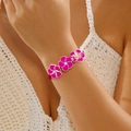 Detail eines handgewebten Armbands mit rosa Frangipani-Blüten und funkelnden Strasssteinen - Fuchsia