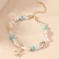 Detail of seashell bracelet with turquoise beads and golden star charm on sandy background - Starfish Conch Turquoise Beaded Bracelet