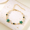 Goldenes Blumenarmband mit Smaragd und Kristallsteinen auf strukturierter Steinplatte - Armband Grün