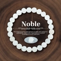 Detail eines weißen Mondstein-Perlenarmbands auf Holz mit Noble-Marketing-Tag - Weißer Jade