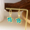 Elegante goldene Ohrringe mit hellblauen Kristallblüten an einem stilvollen Verkaufsständer - Ohrringe Blau