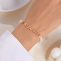 Détail d'un collier de perles Mama avec lettrage doré porté sur un poignet élégant - Bracelet de perles / Or