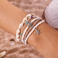 Detail von Strandarmbändern mit silbernen Seesternen, Schildkröten und Muscheln im Sand - Stil 24 / 5-teiliges Set