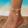 Dreilagiges Boho-Fußkettchen mit weißen Perlen und Muschelanhänger am Strand getragen - 3er Set / Gold & Perlenmuschel-Anhänger