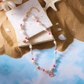 Rosa Muschelkette mit Muschelanhänger und Perle auf beigem Stein und Strandhintergrund - Rosa Perle Muschel Halskette