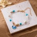 Perlenarmband mit blauem Muschelanhänger und Seemuscheln auf Sand für einen Strand-Look - Blau Emaille Muschel
