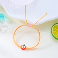 Detail eines handgewebten Armbands in Rosa und Gelb mit einem süßen roten Apfelanhänger - Apfel