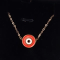 Macro shot of gold Evil Eye pendant with red and white enamel on black velvet background - Orange