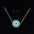 Macro view of gold evil eye pendant with blue enamel sunburst details on black background - Blue