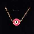 Close-up of golden Evil Eye pendant with pink enamel detail on black velvet background - Rose Red