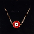 Macro detail of red Evil Eye disc pendant with golden eyelash accents on a fine chain - Red
