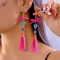 Detail of pink bow and blue skull tassel earrings on model for Halloween style - Rose Red