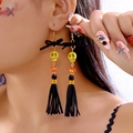 Detail of Halloween skull tassel earrings with black bows and orange beads on model - Black