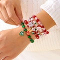 Weihnachts-Perlenarmband-Set mit bunten Anhängern auf weißem Strickpullover-Hintergrund - Rotes Rentier