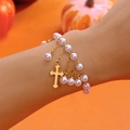 Détail d'un bracelet en perles avec pendentif croix et pompons dorés sur poignet - Bracelet / Bracelet Croix en Perles Or (BR25Y0609-2)