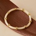 Detailed view of cream acrylic tube beads and gold metal spacers on a wooden display - Milky White Translucent (AB0082-1)