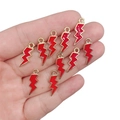 Handheld view of ten red enamel lightning bolt charms with gold metal edges for DIY jewelry - Red