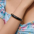 Primo piano di un bracciale rigido in smalto nero con spirali dorate su un polso - Nero