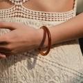 Close-up of translucent amber acrylic bangle on model with white lace dress detail - Amber