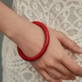 Detailed close-up of a red acrylic bangle with ink textures worn over white lace fabric - Red Ink Texture