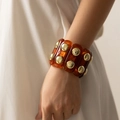 Primo piano del bracciale in resina ambra con borchie dorate sul polso di una modella - Texture Ambra Tartarugato (AB0049-4)