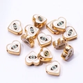 Macro detail of heart-shaped evil eye beads with white enamel and golden plating - White